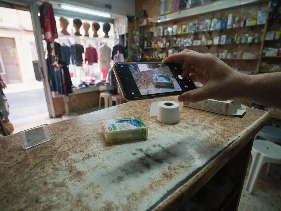 Una mano fotografiando con el movil un producto colocado sobre el mostrador de una tienda de barrio